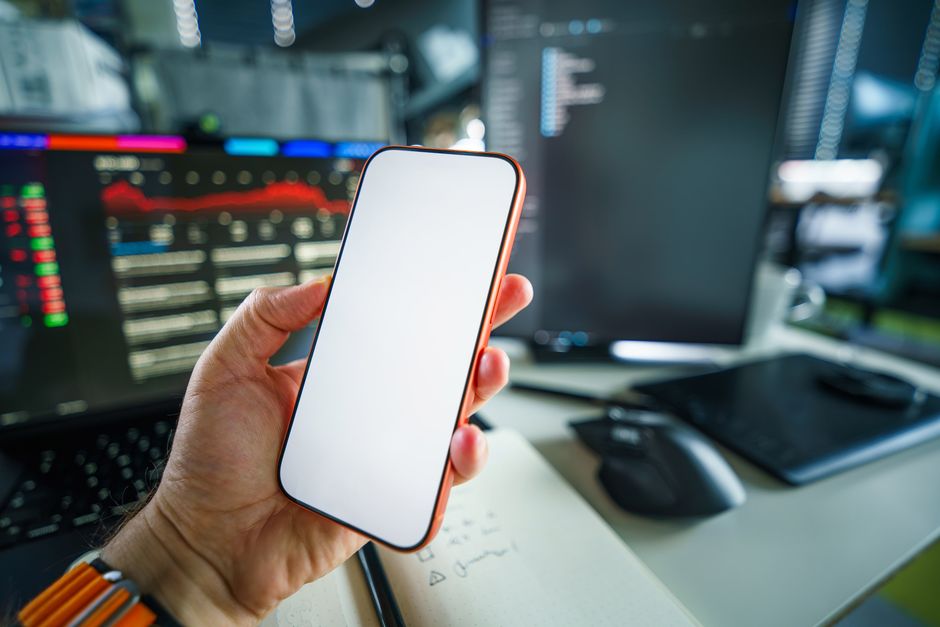 A person holding a smartphone with a blank screen, set within a modern tech office with charts.