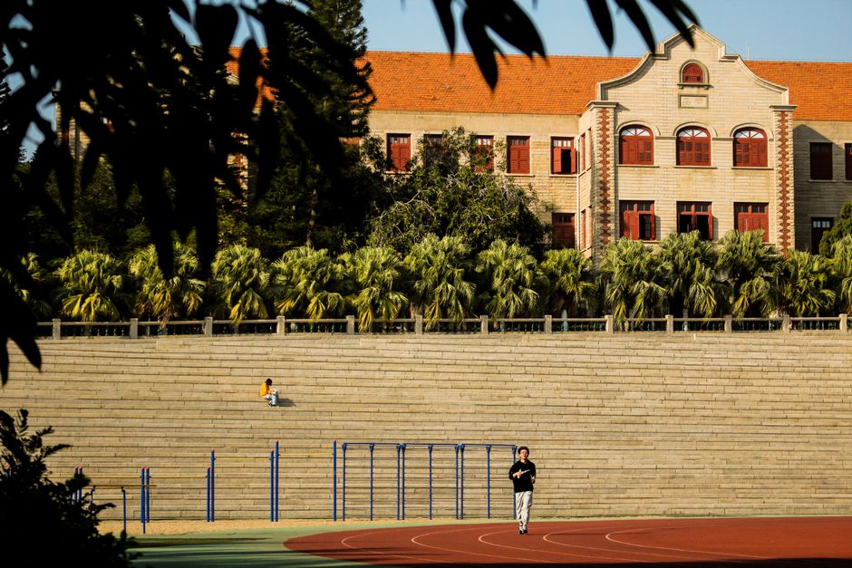 Man jogging on a track by historic university, sunny day.